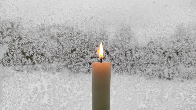 A candle burns against the background of a frozen window №6
