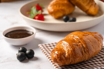 Croissant pastry served on a napkin with a bowl of chocolate sauce and blueberries. A delicious breakfast.