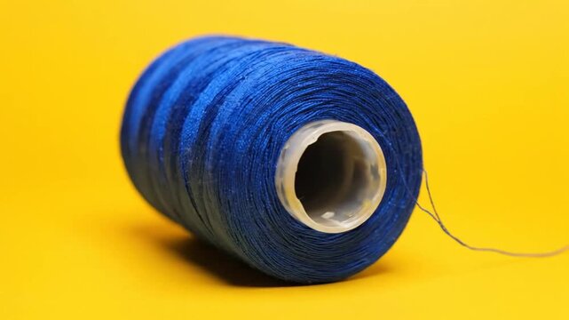 Close-up of a blue thread spool on a vibrant yellow background.