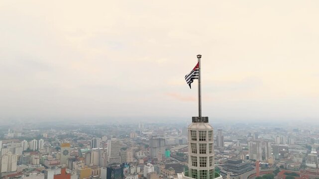 Aerial view pushing in showing overpass with Farol Santander and Sao Paulo flag in Sao Paulo, Brazil. Drone shot revealing Catavento museum in foggy background