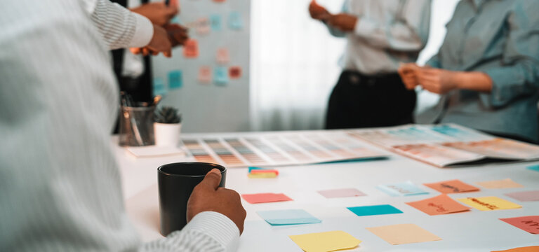 A diverse group of professionals engages in a lively brainstorming session, using colorful sticky notes to share ideas and enhance collaboration in a modern office setting. SACTR