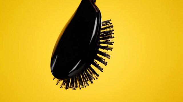 Close-up of a black hairbrush with golden bristles rotating against a vibrant yellow background, showcasing hair care and beauty tools.