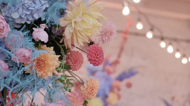 Vibrant floral arrangement featuring pastel dahlias and hydrangeas with string lights in a soft bokeh background.