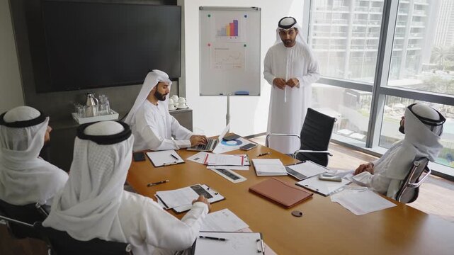 Arab businessmen wearing emirati kandura meeting in office for business deal - Corporate business group of middle-eastern people working in an international company in middle east 