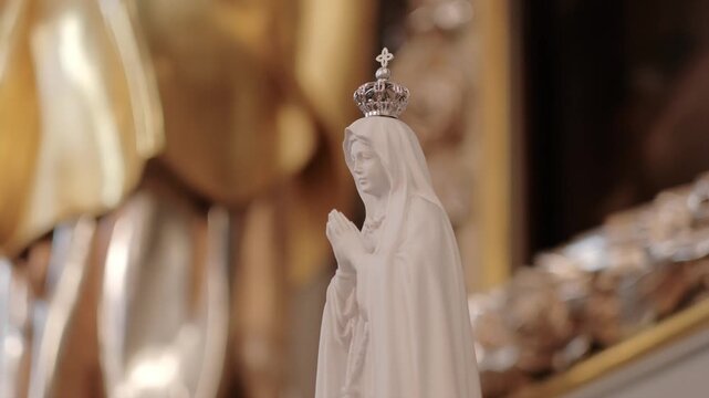 Small white statue of the Virgin Mary praying, adorned with a silver crown in a church setting.