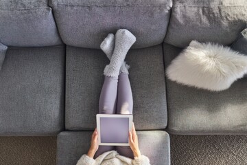 Young caucasian female relaxing on couch with tablet and cozy socks