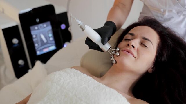 Woman getting a face lifting session with microcurrent device at a modern cosmetology clinic. Expertise in skincare and anti-aging
