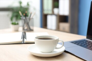 Obraz premium Cup of coffee, laptop and stationery on wooden table in office, closeup
