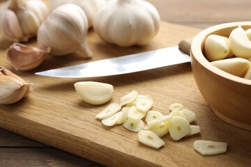 Fresh garlic bulbs, cloves and knife on wooden table, closeup