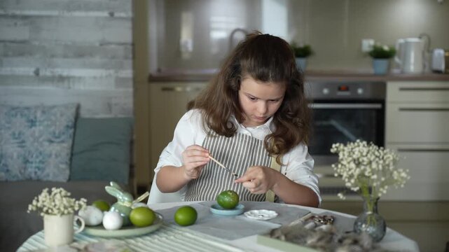 A girl decorating Easter eggs at home, preparing for a family holiday and a spring tradition