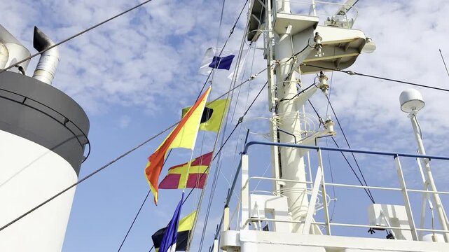 Festive maritime display on a merchant ship showing colorful signal flags raised on halyards against partly cloudy skies to honor a significant marine event and nautical heritage.