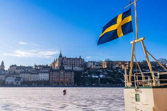 Ice skaters on the lake M&auml;laren in Stockholm, with S&ouml;dermalm in the background and the swedish flag in the foreground