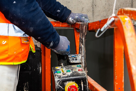 Close up of construction worker operating scissor lift control panel while performing interior painting work inside industrial warehouse.