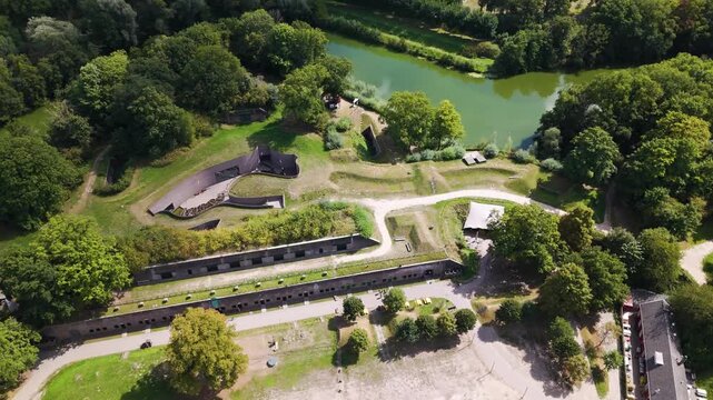 layered earthen ramparts curved defensive walls preserved bunkers winding gravel paths surrounded by dense trees calm green waterways historic riverside fortifications roman fort castellum fectio 
