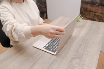 Woman opening a modern slim laptop on a wooden desk in a home office.