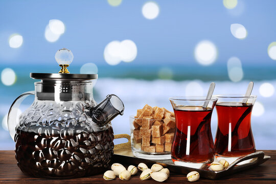 Tasty Turkish tea, sugar and pistachios on wooden table against blurred seascape