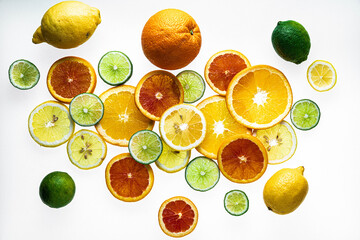 Lemon, lime and orange slices and whole fruit scattered against a white surface.