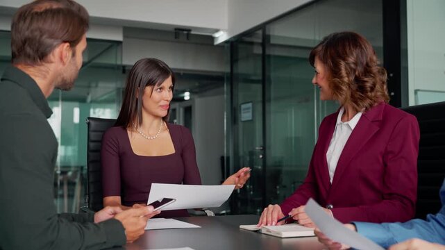 Team of young European business man and Latin business woman discussing project sitting at table in office. Business people work together. Female mentor leader coach have meeting with colleagues