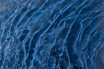 Water with a shining rippled texture on a dark blue background. Abstract Water surface background idea. Abstract summer water background.  © Maja 