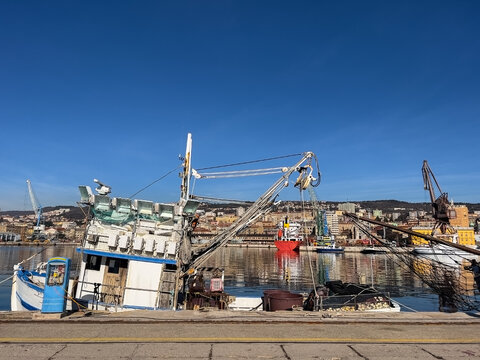 Traditional fishing boat equipped nets moored in the port of Rijeka, industrial maritime scene under blue sky.