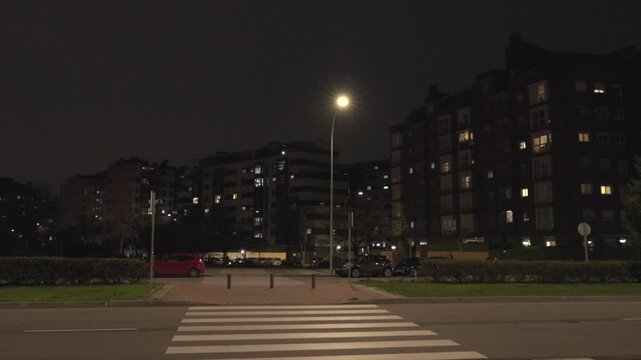 A street scene at night with a red car parked on the left side of the street