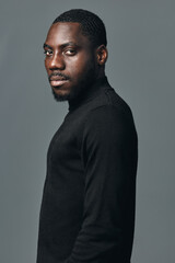 Obraz premium African man portrait in creative conceptual visual style wearing black turtleneck sweater against gray background. Confident male model with dark skin and short hair looking at camera in studio.
