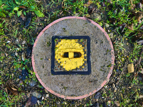 A striking, top-down study of a yellow gas utility marker at Pongratz Gergely ter. The bold geometric contrast between the yellow metal, grey concrete, and surrounding green grass offers a vibrant