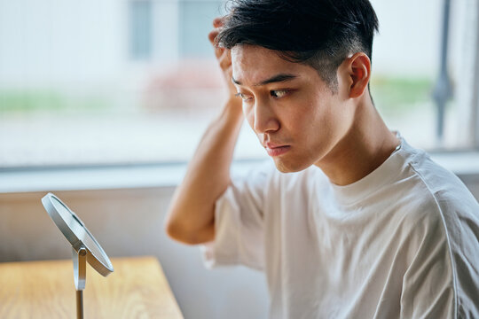 Young man styling hair in front of mirror during morning grooming routine at home