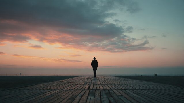 Man walking on boardwalk at sunset