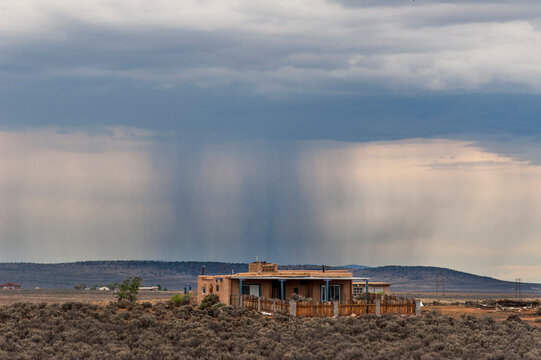 USA, New Mexico, Carson.  Rain falling in the distance behind adobe house on the mesa.