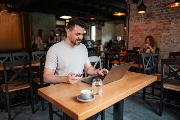 Fototapeta premium Freelancer working on laptop and using smartphone in cafe