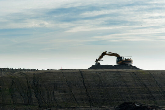 Canada, BC, Delta.  Excavator silhouetted against sky atop construction site preload.