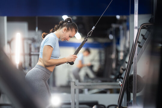 Determined young woman performing triceps pushdown at gym