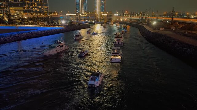 A stunning nighttime view of Dubai Marina, with illuminated luxury yachts and boats cruising the canal. Modern skyscrapers create a dazzling backdrop for this glamorous, urban nightlife scene.

