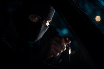 Masked criminal holding knife inside car at night