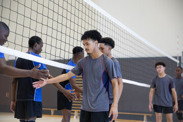 African American teen males lining up shaking hands across volleyball net in gym, gray blue jerseys