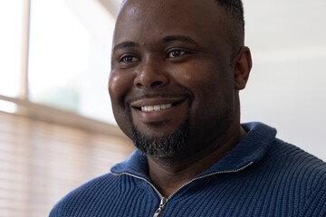 Obraz premium African American man smiling wearing blue ribbed zip sweater facing window blinds at home