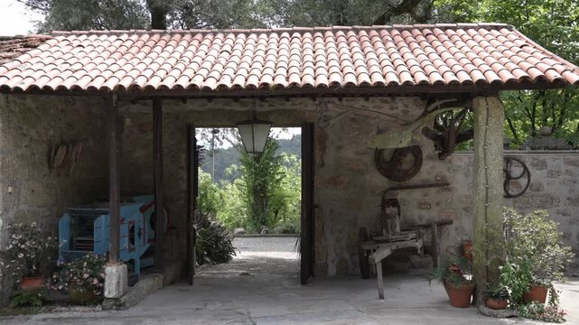 Stone outbuilding with clay tile roof open doorway tools plants and lantern