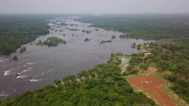 Luxury safari lodge complex with an airstrip beside the Nile River surrounded by dense woodland and river islands in Murchison Falls National Park, Uganda, drone pull out and reveal.