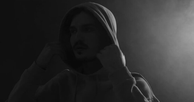 Man in hood on dark background with smoke, camera moving up. Black and white effect