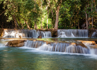 Obraz premium Huay Mae Khamin Waterfalls cascading through lush tropical forest in Kanchanaburi, Thailand. Clear water streams over rocky terrain. Surrounded by dense greenery and tall trees.