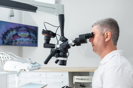 Dentist using dental microscope treating patient teeth at dental clinic office. Medicine, dentistry and health care concept. Dental equipment