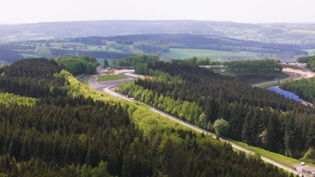 belgium f1 formula one circuit winds through ardennes forest asphalt bends eau rouge safety barriers distant grandstands rolling countryside belgian grand prix near spa francorchamps 