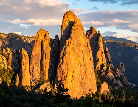 Jagged, sunlit rock formations amidst mountain greenery at dusk