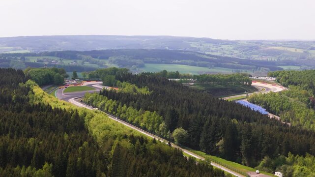 belgium f1 formula one circuit sweeps through ardennes forest eau rouge section carving bends asphalt bordered by safety barriers grandstands countryside hills spa francorchamps 