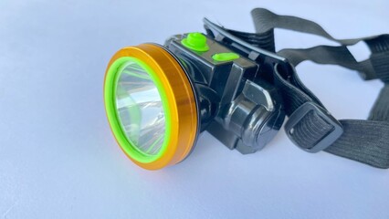 A headlamp with a black elastic strap and green and yellow accents. This close-up photo against a white background shows details of the portable lighting device.