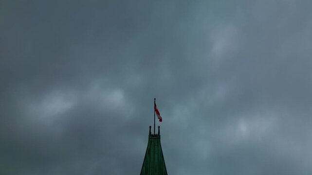 Ottawa Hill Clock Tower closeup drone shot of the Canadian Flag against and down to the clock on a cloudy summer sky conveying an atmosphere of gloom and political worry.