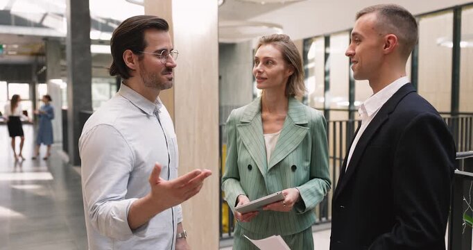 Group of businesspeople lead business related conversation standing in office hallway, shaking hands, expressing respect. Completion of successful agreement, professional cooperation and partnership