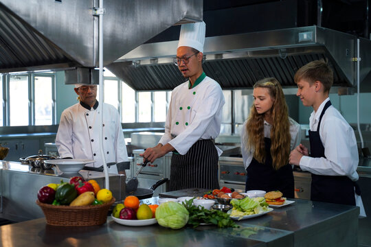 Chef teacher teaches cooking to the group children in class kitchen room.  Chef preparing student for learning marking and cooking food at workshop.  Education Concept