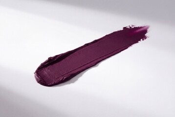 Fototapeta premium Deep plum purple lipstick swatch with creamy matte texture on white background